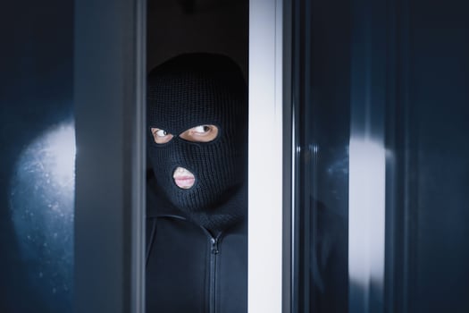 Intrusion Concept. Villain with black hat sneaking into house through open glass door, searching with flashlight photo