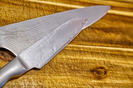 Close-up of a sharp kitchen knife resting on a wooden cutting board, showcasing the blade's edge and texture. photo