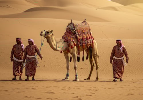 Walking Camel with Arab Men in Traditional Dress Across Desert Dunes photo