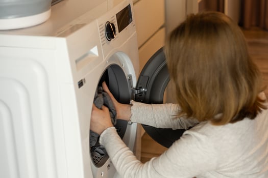 Woman loading laundry into a washing machine in a modern home kitchen while preparing for household chores photo