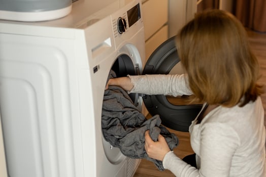 Woman doing laundry in a modern home while loading a washing machine with clothes in the living area photo
