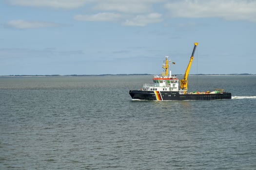 A utility vessel navigates smooth waters near a coastal region on a clear day, showcasing efficient marine operation and maintenance activities photo