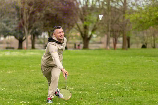 A man in a beige tracksuit plays badminton in the park photo