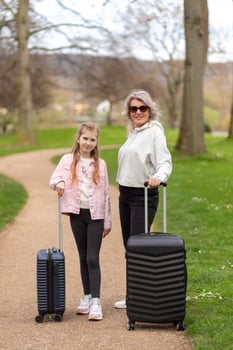 Woman and girl smiling and posing with suitcases against the backdrop of a spring park. photo