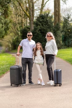Family of three walking in park with suitcases photo