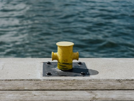 A yellow mooring bollard on a pier with a blurred water surface in the background. photo