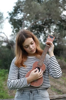 Girl Practices With Ukulele Musical Instrument In The Countryside During A Break photo