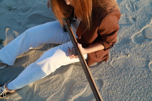 Girl Plays The Bass Instrument Sitting On The Beach At Sunset Near The Ocean photo