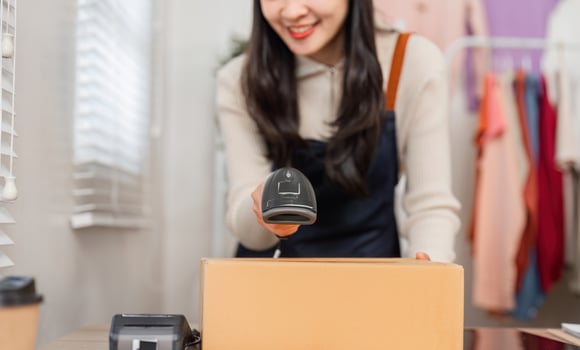Diverse young woman scanning a cardboard box with a barcode scanner in retail. photo