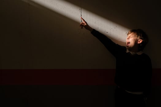 Preteen boy standing in sunbeam screaming and pointing finger photo