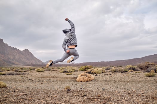 Carefree man traveler jumping on rocky ground near hills photo