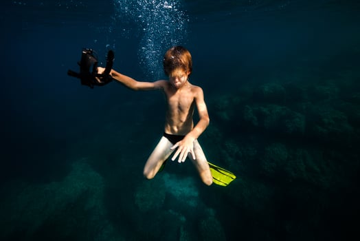 Teen boy swimming underwater of ocean with closed eyes photo