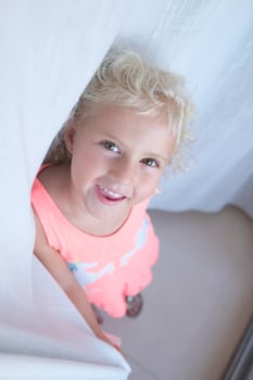 Smiling little girl standing near curtain at home photo
