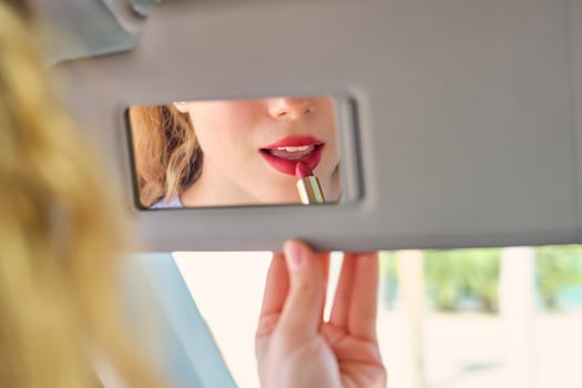 Crop young woman applying red lipstick against mirror in car photo