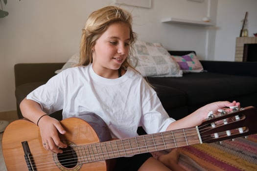Cute girl sitting on floor while tuning wooden guitar photo