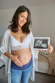 Smiling pregnant woman holding sonogram in living room photo