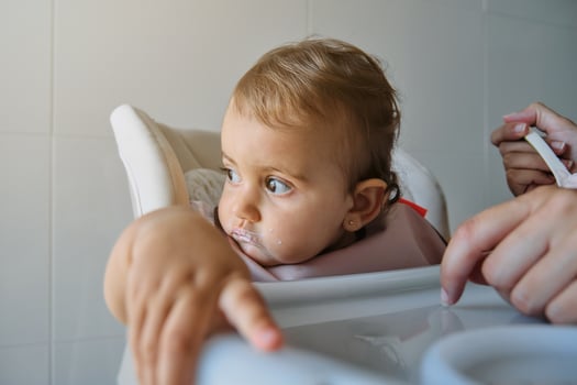 Unrecognizable woman feeding daughter on high chair with spoon photo