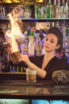 Female barkeeper making fire over cup while mixing cocktail photo