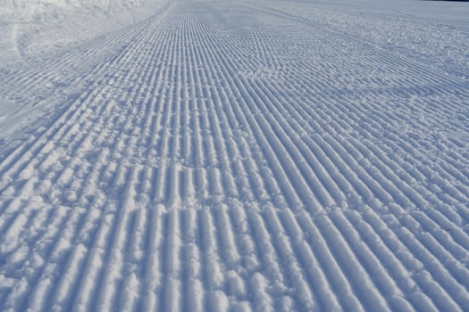 A groomed snow track at a ski resort features fresh white snow and clear track marks from skiers and snowboarders, capturing the thrill of winter sports in a picturesque landscape. photo
