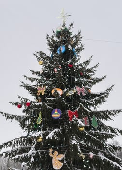 A beautifully decorated Christmas tree covered in fresh snow stands against a winter sky. Colorful ornaments, glowing lights, and a shining star at the top create a festive holiday atmosphere photo