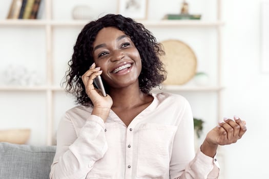 Smiling Black Woman Talking On Mobile Phone At Home With Her Boyfriend, Having Pleasant Conversation, Enjoying Mobile Communication, Speaking With Friends Via Cellphone And Laughing, Copy Space photo