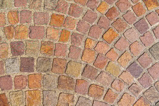 The image features a red cobblestone street pavement texture. Each stone varies in shade and showcases a classic herringbone pattern, giving it an old and weathered charm. photo