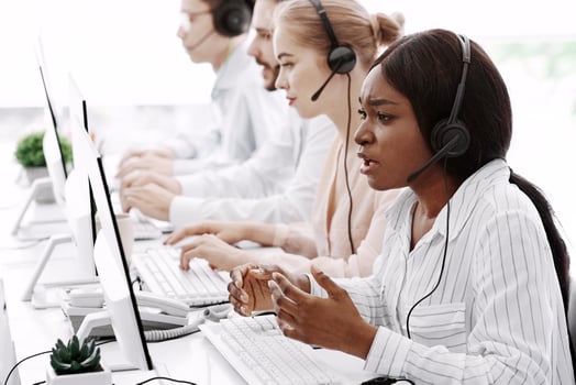 Stressed call center manager with headset listening to clients complaint and her team at office photo