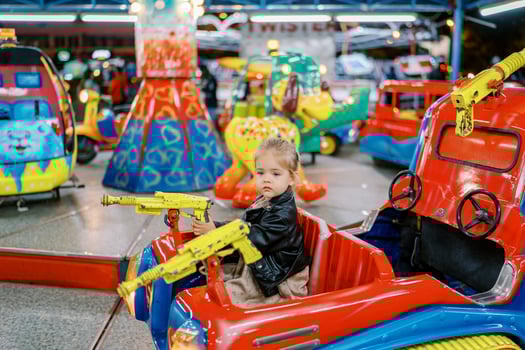 Little girl rides a toy tank on a carousel holding a pistol steering wheel photo