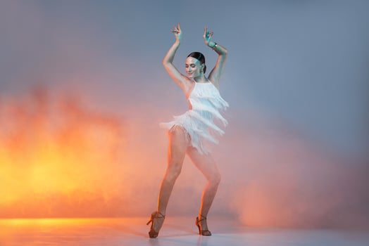 Elegant female Latin dancer in a white fringed dress performing a dynamic move with grace and confidence in artistic lighting photo