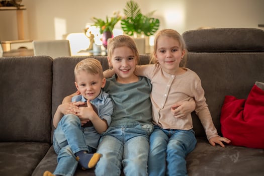 portrait of three children at home. brother and sisters sit on the couch hugging and smiling photo