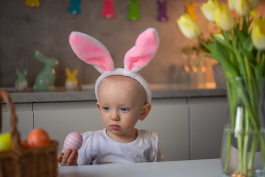 happy cute little baby girl wearing bunny ears on easter day sitting at the table in the kitchen photo