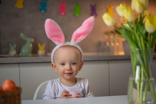 happy cute little baby girl wearing bunny ears on easter day sitting at the table in the kitchen photo