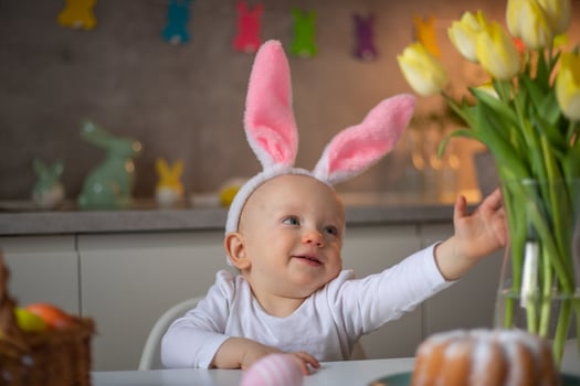 happy cute little baby girl wearing bunny ears on easter day sitting at the table in the kitchen photo