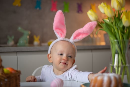 happy cute little baby girl wearing bunny ears on easter day sitting at the table in the kitchen photo