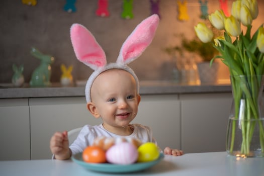 happy cute little baby girl wearing bunny ears on easter day sitting at the table in the kitchen photo