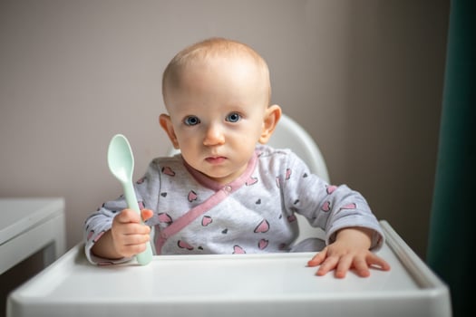 Happy baby girl with spoon sitting in highchair at home photo