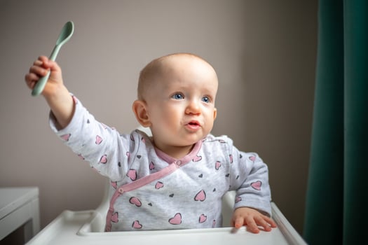 Happy baby girl with spoon sitting in highchair at home photo