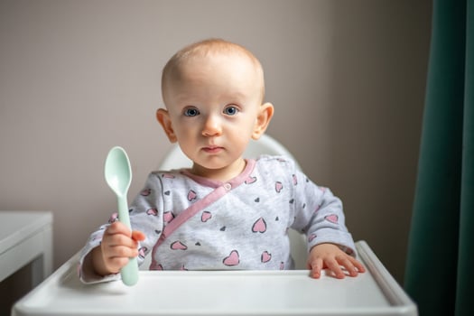 Happy baby girl with spoon sitting in highchair at home photo