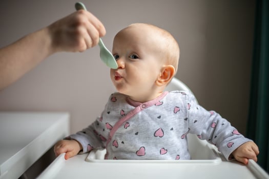 Baby girl eating blend mashed food sitting, on high chair, mother feeding child, hand with spoon for vegetable lunch, baby weaning, first solid food for young kid photo