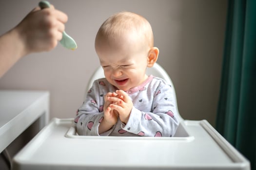 Llittle baby does not want to eat first complementary food. Disgruntled child at highchair photo