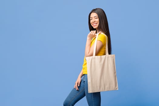 Eco-Friendly Lifestyle. Cheerful Asian Girl Posing With Blank Tote Eco Bag Over Purple Studio Background, Copy Space photo