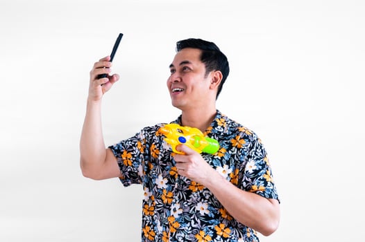 Thai male do selfie from smartphone with colorful shirt and blurred focus of water gun for Thailand Songkran festival concept. photo