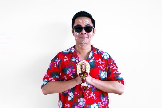 Thai male with white clay filler on face wearing colorful shirt doing pray pose with garland for Songkran or Water festival in Thailand concept. photo