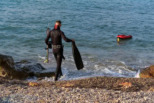 Anonymous man in wetsuit walking in seawater with flippers and speargun photo