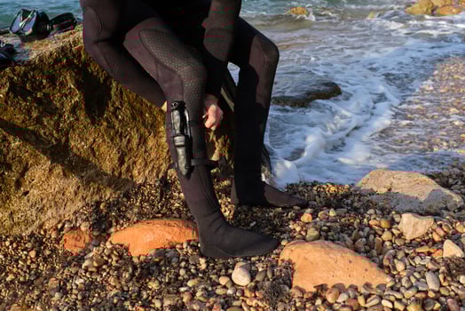 Anonymous crop man sitting on stone and fastening knife to leg photo