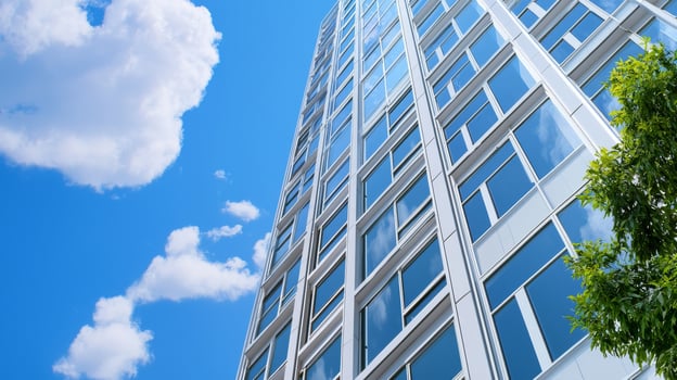 A modern high-rise building with large glass windows, surrounded by greenery and under a clear blue sky. photo