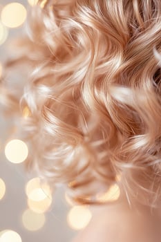 Close-up view capturing the beauty of healthy, defined natural curls being hydrated with a nourishing mist. A soft-focus background creates a warm, radiant aesthetic photo