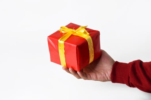 A hand of a person wearing a red sweater holds and shows a red gift box photo