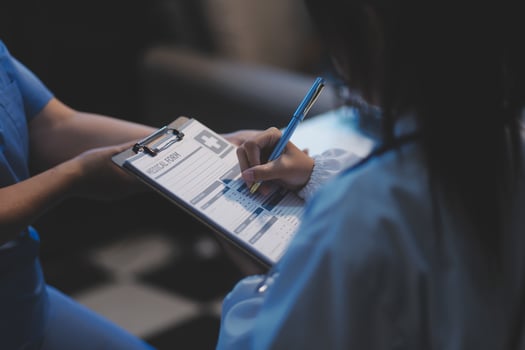 A nurse is writing on a clipboard while another person looks on photo