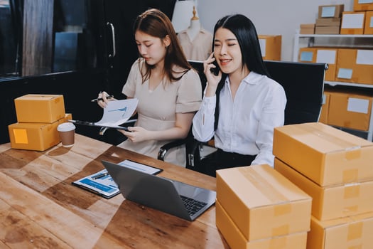 Two women sitting at a table with boxes and papers photo